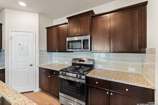 kitchen with light stone counters, backsplash, light wood-style floors, appliances with stainless steel finishes, and dark brown cabinets