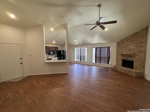 unfurnished living room featuring lofted ceiling, a fireplace, ceiling fan, and dark wood finished floors