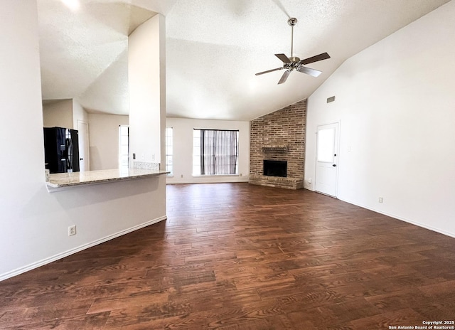 unfurnished living room featuring a textured ceiling, dark wood finished floors, baseboards, a brick fireplace, and ceiling fan