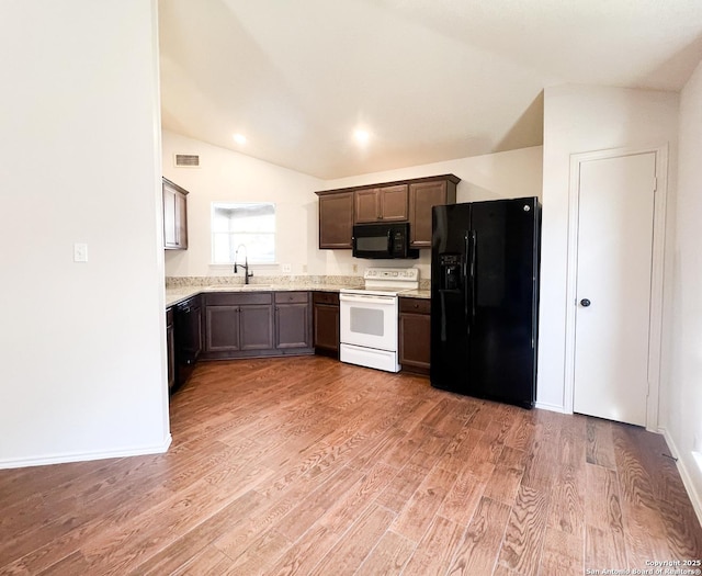 kitchen featuring visible vents, light wood finished floors, lofted ceiling, a sink, and black appliances