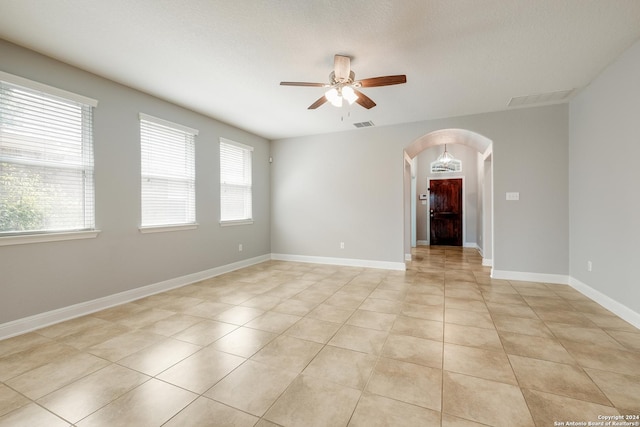 unfurnished room with visible vents, arched walkways, light tile patterned floors, baseboards, and ceiling fan