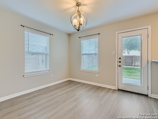 interior space with a notable chandelier, light wood-style flooring, and baseboards