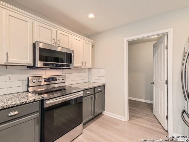 kitchen featuring gray cabinetry, appliances with stainless steel finishes, light wood finished floors, decorative backsplash, and baseboards