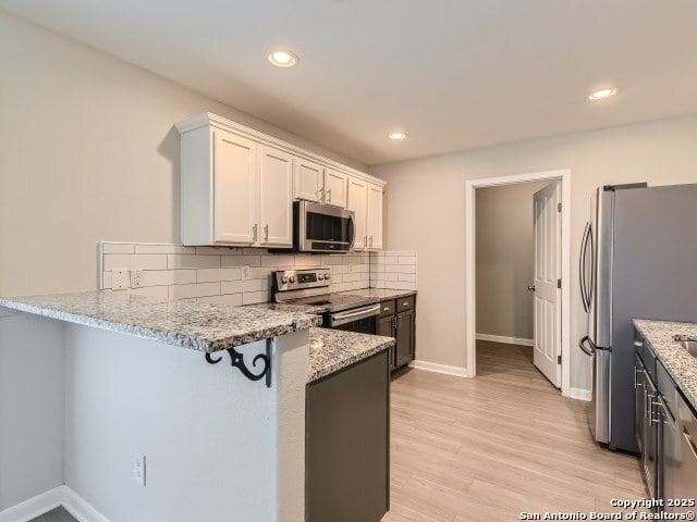 kitchen with a peninsula, backsplash, light stone countertops, and appliances with stainless steel finishes