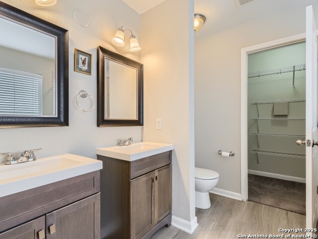 bathroom with a sink, baseboards, toilet, and two vanities