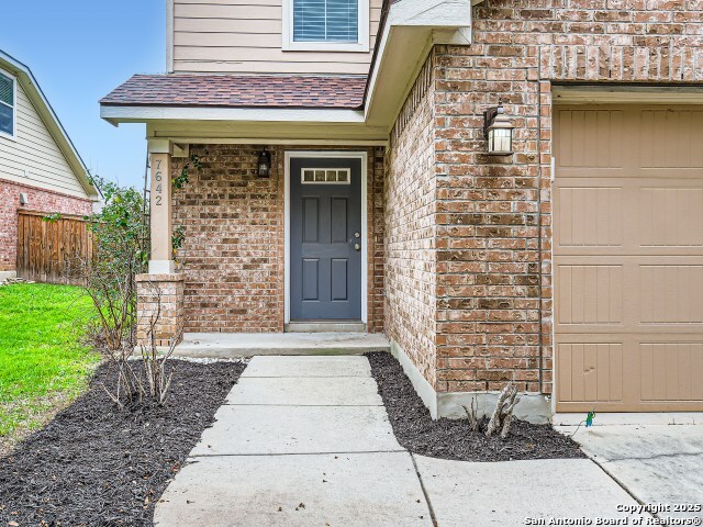 doorway to property with fence, brick siding, and a shingled roof