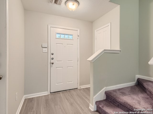 foyer with stairway, baseboards, visible vents, and light wood-type flooring