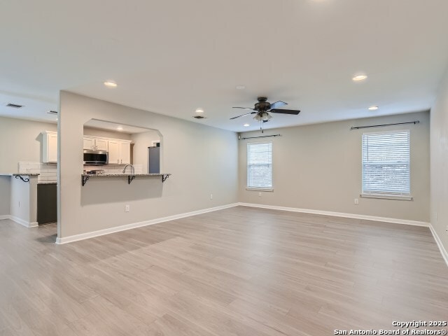 unfurnished living room with baseboards, recessed lighting, light wood-style flooring, arched walkways, and a ceiling fan