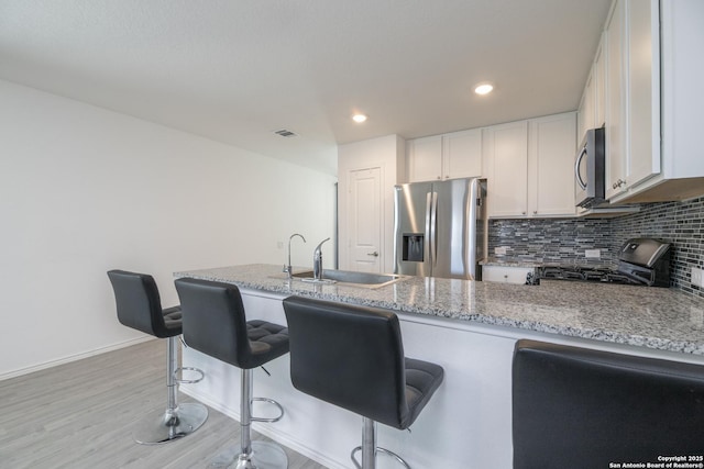 kitchen with light stone countertops, a sink, appliances with stainless steel finishes, white cabinetry, and tasteful backsplash