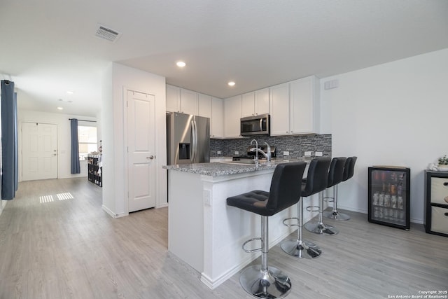 kitchen with visible vents, a peninsula, a sink, stainless steel appliances, and wine cooler