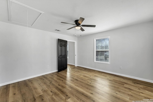 empty room with wood finished floors, baseboards, visible vents, attic access, and ceiling fan