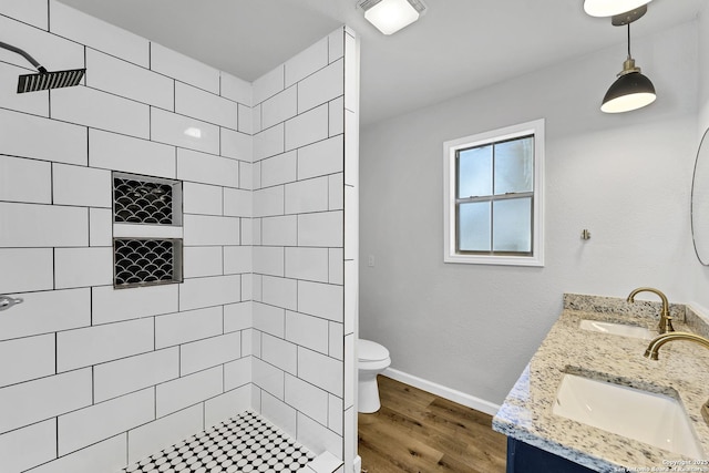 bathroom featuring a sink, tiled shower, toilet, and wood finished floors