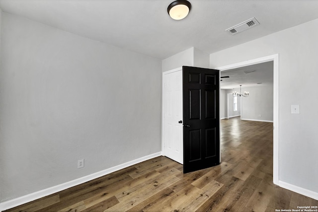 empty room featuring visible vents, baseboards, wood finished floors, and a chandelier