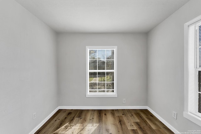 unfurnished room featuring plenty of natural light, baseboards, and wood finished floors