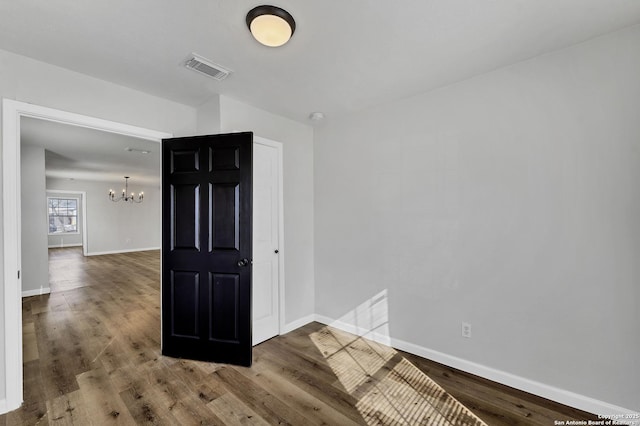 empty room with a notable chandelier, wood finished floors, visible vents, and baseboards