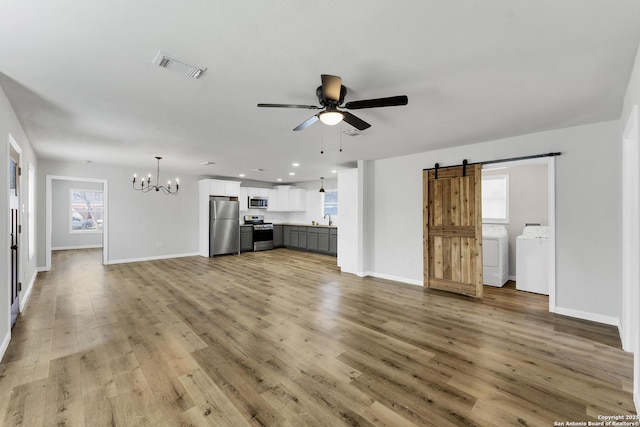 unfurnished living room with visible vents, ceiling fan with notable chandelier, a barn door, light wood finished floors, and washing machine and clothes dryer