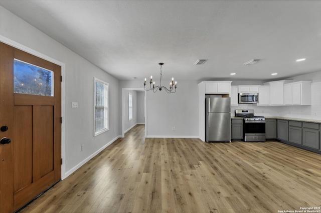 kitchen with stainless steel appliances, light wood-style floors, white cabinets, baseboards, and a chandelier