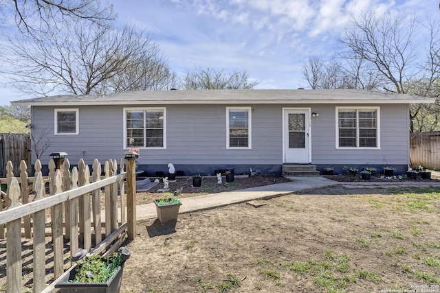 rear view of property featuring entry steps, a vegetable garden, and fence