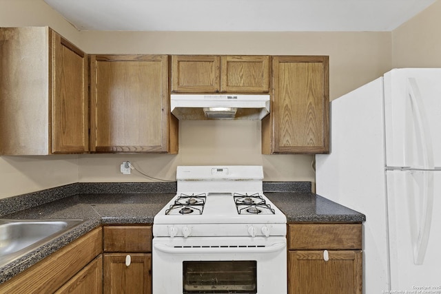 kitchen with white appliances, dark countertops, brown cabinets, and under cabinet range hood