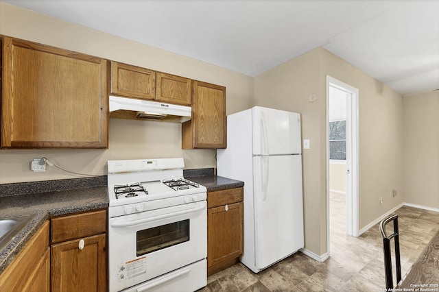 kitchen with dark countertops, baseboards, under cabinet range hood, brown cabinetry, and white appliances