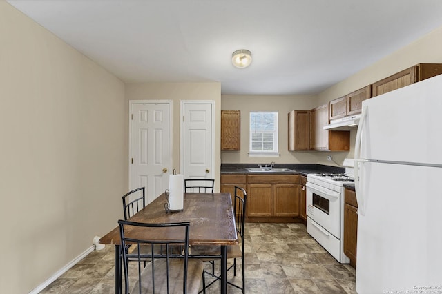 kitchen with under cabinet range hood, a sink, dark countertops, white appliances, and baseboards