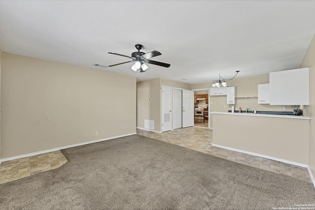 unfurnished living room featuring visible vents, ceiling fan with notable chandelier, baseboards, and light carpet