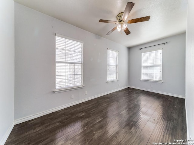 spare room with dark wood-type flooring, a ceiling fan, and baseboards