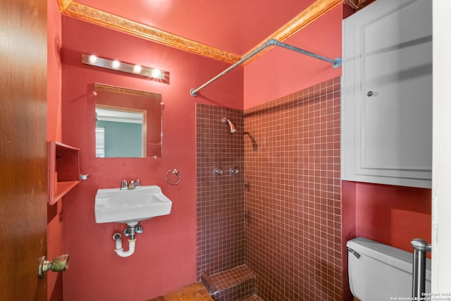 bathroom featuring toilet, tiled shower, and a sink