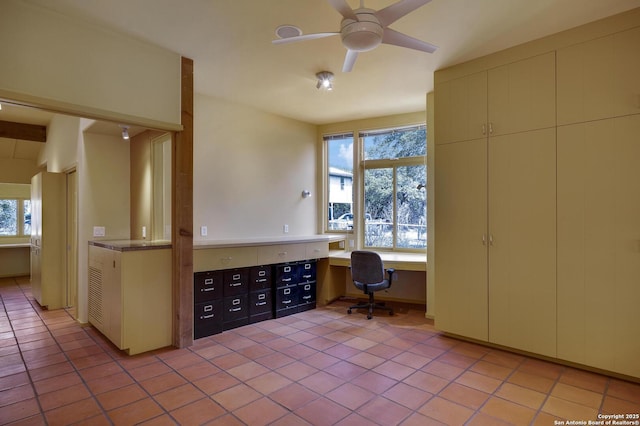 unfurnished office with light tile patterned floors, built in desk, and a ceiling fan