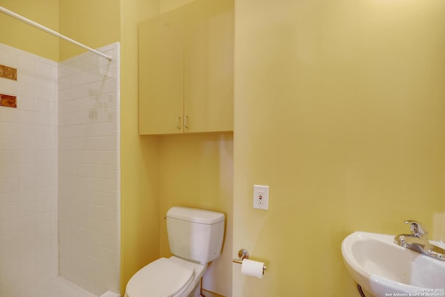 bathroom with toilet, a tile shower, and a sink