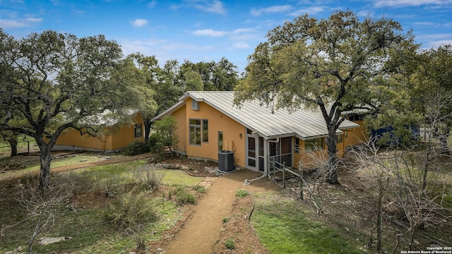 back of property featuring central AC unit, stucco siding, metal roof, and a standing seam roof