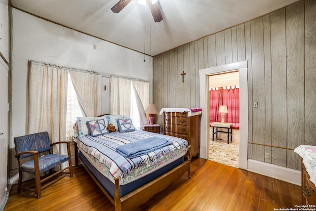 bedroom with wooden walls, ceiling fan, and wood-type flooring