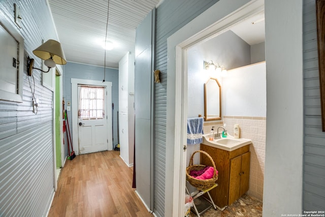 hallway with light wood-style flooring, tile walls, and a sink