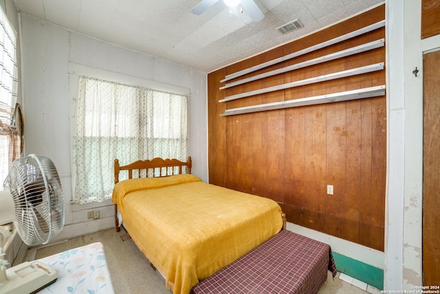 carpeted bedroom featuring a ceiling fan, visible vents, and wood walls