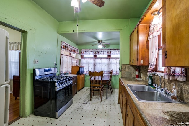 kitchen with brown cabinetry, a ceiling fan, stainless steel range with gas cooktop, and a sink