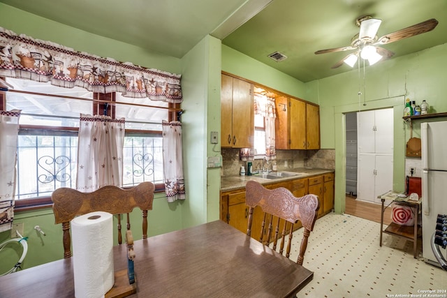 kitchen featuring visible vents, ceiling fan, freestanding refrigerator, brown cabinetry, and a sink