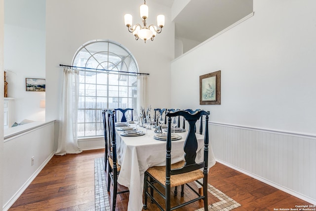 dining area with an inviting chandelier, a high ceiling, dark wood-style floors, and wainscoting