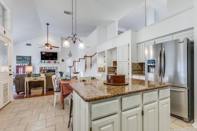 kitchen with a kitchen island, decorative backsplash, dark stone countertops, stainless steel fridge, and a ceiling fan