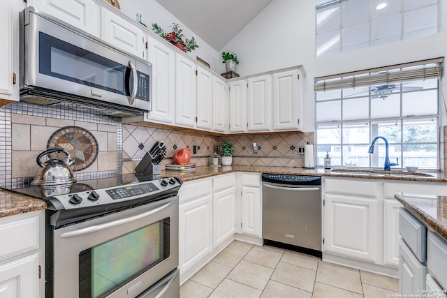 kitchen with white cabinetry, vaulted ceiling, stone counters, and stainless steel appliances