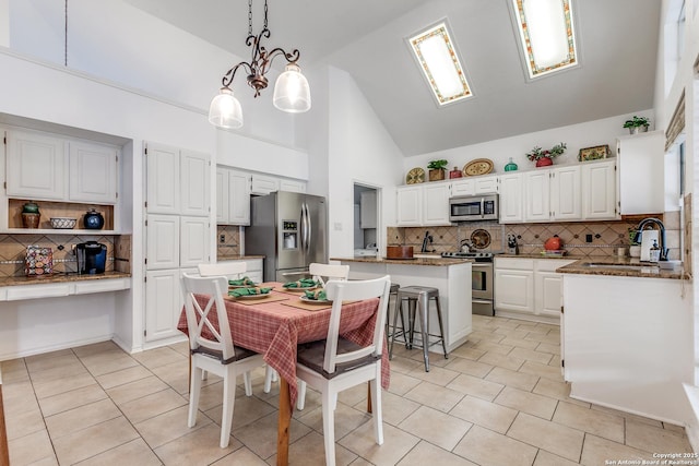 kitchen featuring dark stone countertops, a kitchen island, a sink, stainless steel appliances, and white cabinetry