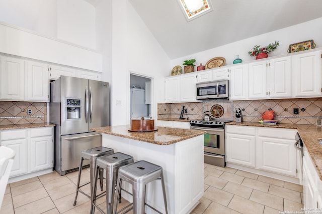 kitchen featuring a kitchen bar, light stone counters, a kitchen island, white cabinetry, and stainless steel appliances