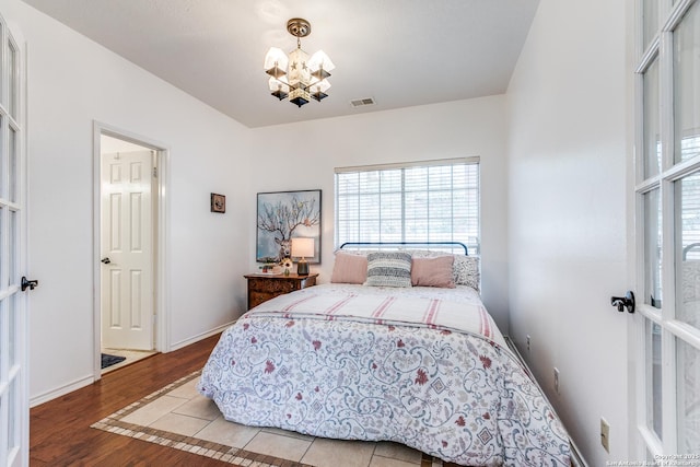 bedroom featuring a chandelier, visible vents, baseboards, and wood finished floors