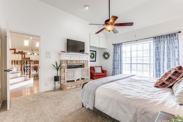 carpeted bedroom with vaulted ceiling, a brick fireplace, and a ceiling fan