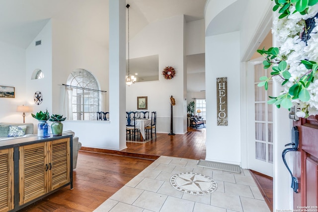 foyer featuring a notable chandelier, high vaulted ceiling, visible vents, and wood finished floors