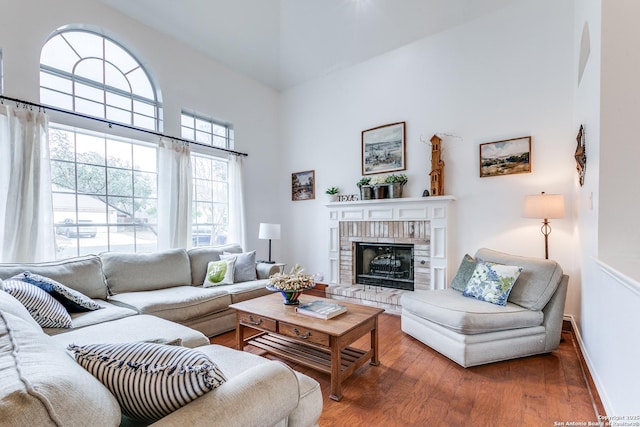 living room featuring baseboards, a high ceiling, a brick fireplace, and wood finished floors