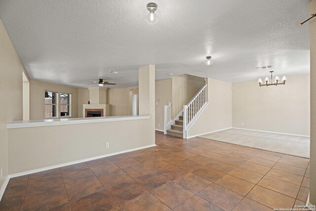1967 Club Xing, New Braunfels, TX 78130 - unfurnished living room with a tiled fireplace, ceiling fan with notable chandelier, a textured ceiling, baseboards, and stairs