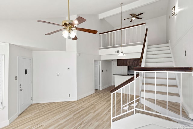 stairs with baseboards, ceiling fan, beam ceiling, wood finished floors, and high vaulted ceiling