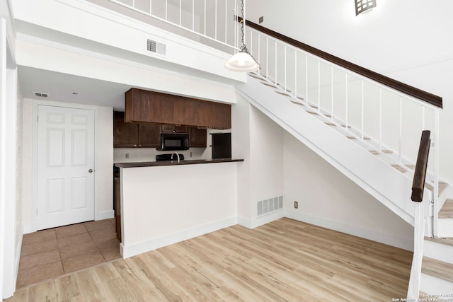 kitchen with visible vents, dark brown cabinets, light wood-style flooring, and black microwave