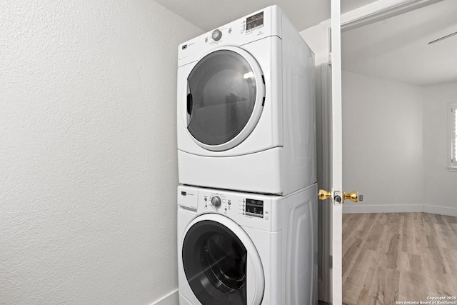 laundry room with laundry area, wood finished floors, stacked washer and clothes dryer, and baseboards