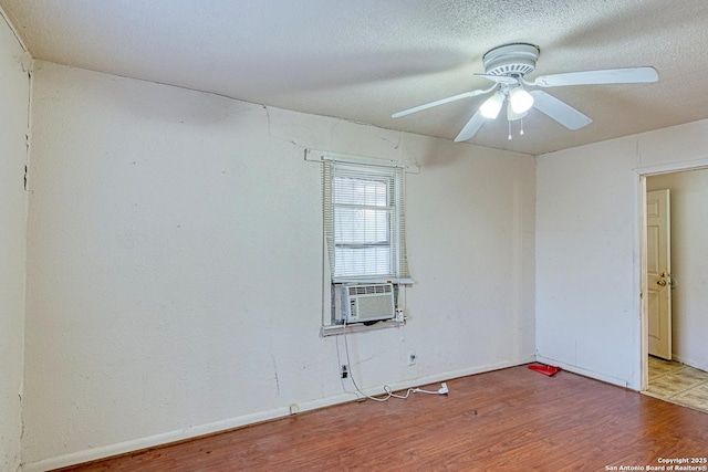 unfurnished room with a textured ceiling, wood finished floors, cooling unit, baseboards, and ceiling fan